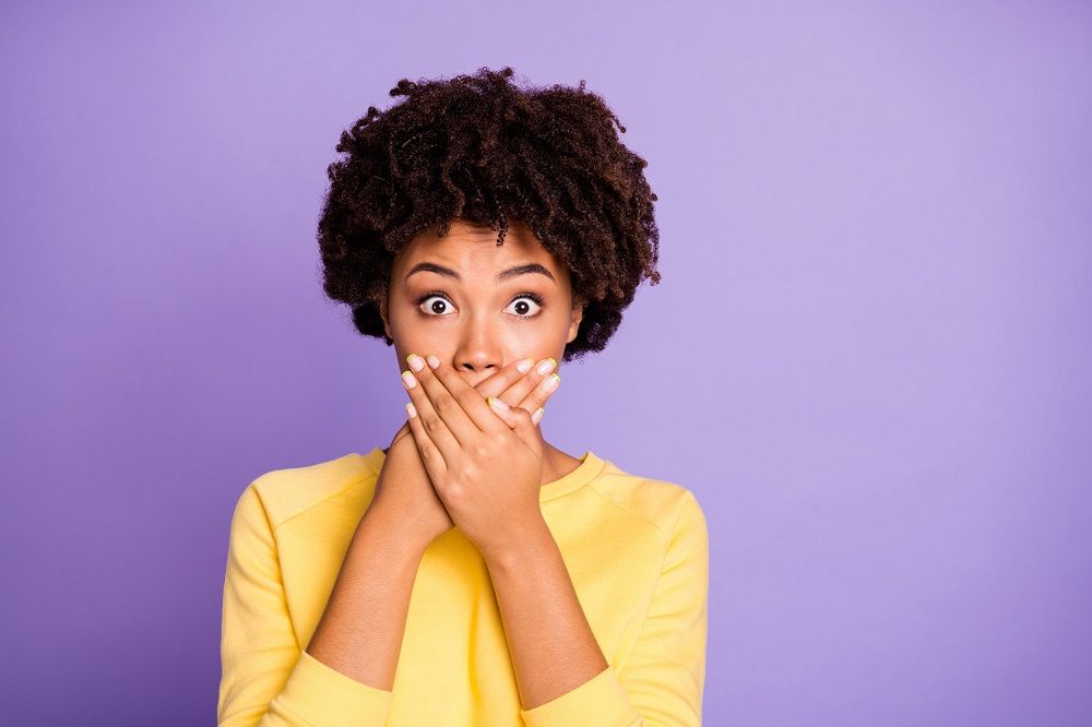 Woman holding both hands over her mouth in shock or surprise on a purple background dental issues preventative dentistry dentist in Burlington North Carolina